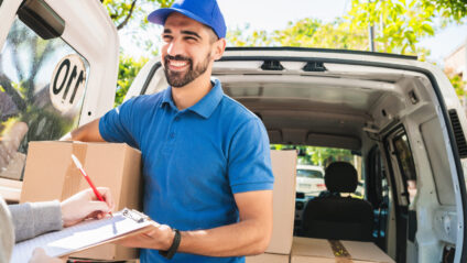 Portrait of a delivery man carrying packages while customer putting signature in clipboard. Delivery and shipping concept.
