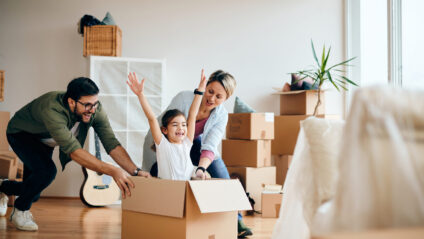 Playful parents pushing their daughter cardboard box and having fun at new apartment.